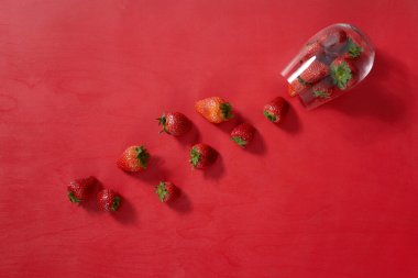 Kırmızı arka planda cam içinde kırmızı tatlı olgun çilekler. Tatlı yaz doğal böğürtlen.