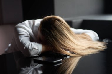 Genç, sarışın, yorgun iş kadını beyaz bir gömlek giyiyor. Mola veriyor ve dizüstü bilgisayarda uyuyor..                               