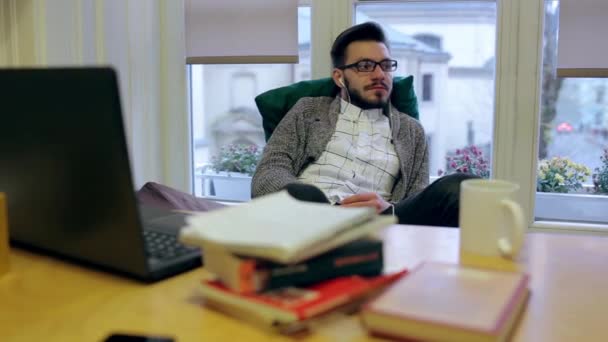 Молодой человек слушает музыку на своем рабочем месте — стоковое видео