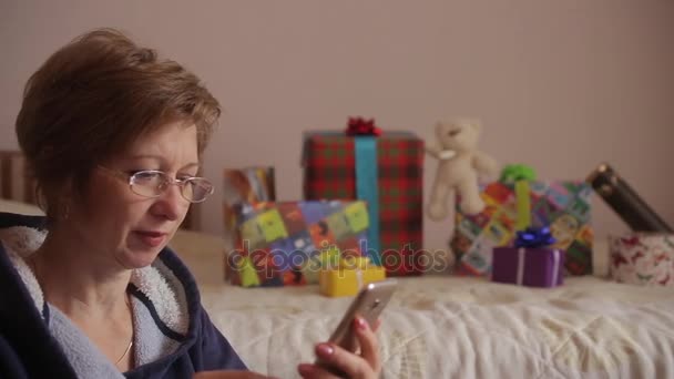 Woman with gifts in background using smartphone to shopping online. — Stock Video