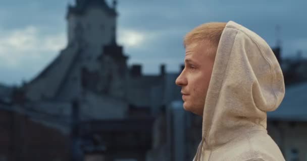 Portrét muže na střeše při západu slunce v kapuci vypadá sebevědomě ve starém městě pozadí — Stock video
