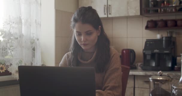 Mulher atraente trabalhando de casa em um computador portátil na cozinha doméstica — Vídeo de Stock