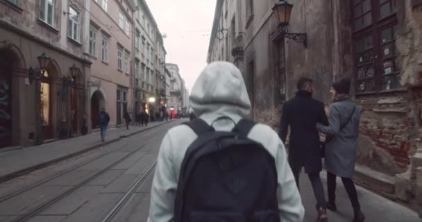 Un hombre caminando por la calle de la ciudad. Un joven con capucha afuera. Vista trasera del hombre caminando por la calle urbana . — Vídeo de stock