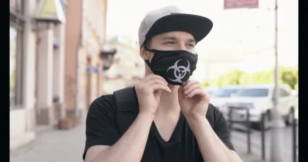 한 남자가 길을 걷다가 질병 바이러스를 퍼트리는 것을 막기 위해 생물학적 위험 로고로 마스크를 쓰고 있다 — 비디오