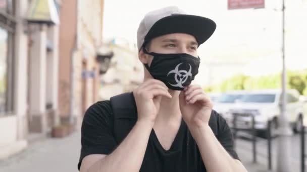 Een man met een masker met biologisch gevarenlogo dat beschermt tegen de verspreiding van het virus Covid-19 tijdens het lopen op straat — Stockvideo