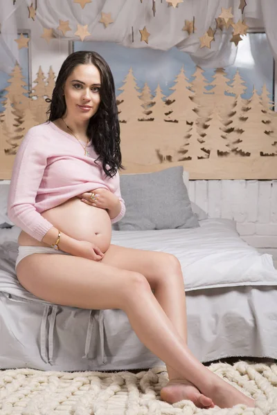 Brunetka w ciąży siedzi na krawędzi łóżka — Zdjęcie stockowe