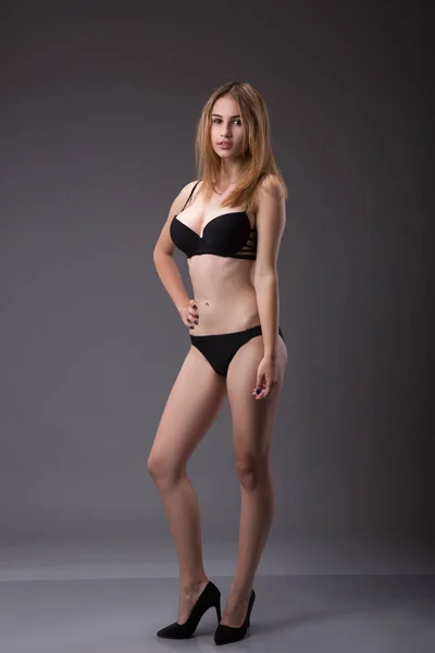 Mujer en forma impresionante en una lencería negra o ropa interior posando sobre fondo gris en un estudio . — Foto de Stock