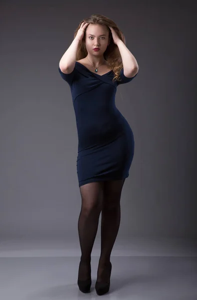 Portrait of a plus size female model posing in black dress over grey background. — Stock Photo, Image