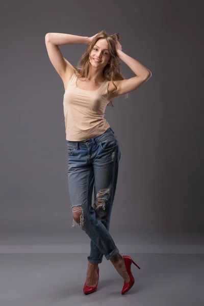 Estúdio retrato de modelo mulher bonita com corpo incrível pernas longas inclinando-se agains parede vestindo jeans jeans, lingerie top salto alto segurando jacker olhando para a câmera . — Fotografia de Stock