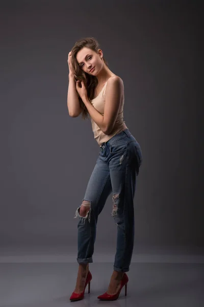 Estúdio retrato de modelo mulher bonita com corpo incrível pernas longas inclinando-se agains parede vestindo jeans jeans, lingerie top salto alto segurando jacker olhando para a câmera . — Fotografia de Stock