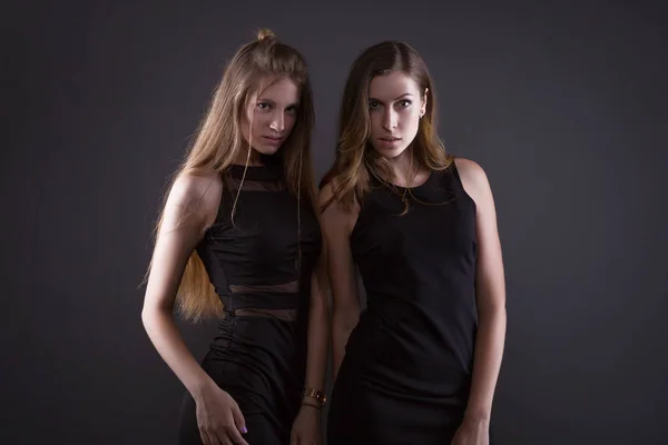 Δύο όμορφες γυναίκες στη μαύρη νύχτα μόδας φόρεμα θέτοντας σε ένα γκρίζο φόντο. — Φωτογραφία Αρχείου