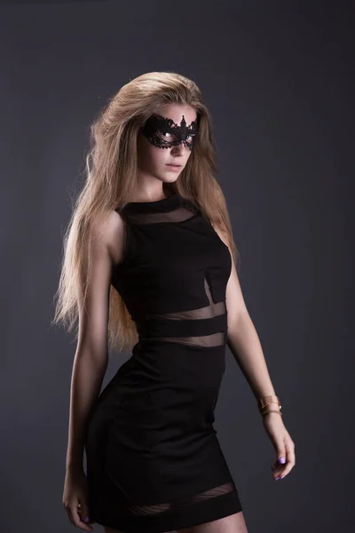 Jovem mulher com máscara de renda preta nos olhos. Vestido preto, cabelo solto. O fundo escuro — Fotografia de Stock