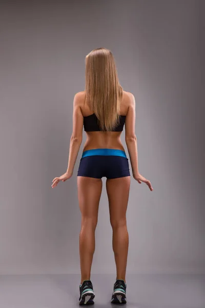 Femme sportive en haut et short posant sur fond gris, pleine longueur. vue de l'arrière . — Photo