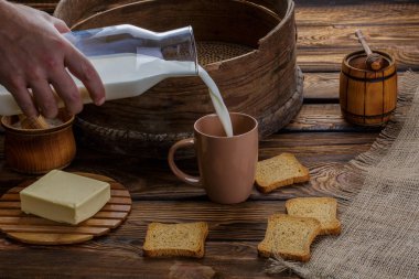 Bir adamın elini çuval bezi ve ahşap arka plan arka plan üzerine kaba süt dökülen. Dağınık kraker