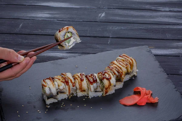 Sushi - Roll na černém plátu s mužem ruka drží hůlky na černém pozadí — Stock fotografie