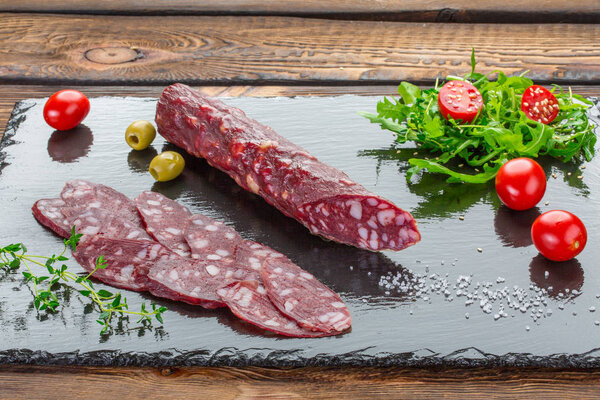 Традиционная салями, нарезанная на темной доске. Вид сверху с копировальным пространством на деревянном фоне
.