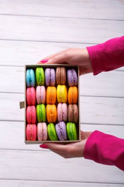 Hediye kutusu beyaz ahşap arka planda, üstten görünüm lezzetli macaroons ile holding eller.