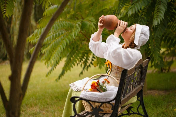 bir köylü kadın küçük bir kapak üzerinde oturan bir sürahi gelen süt içiyor