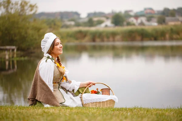 En bonde kvinna med en korg sitter vid floden — Stockfoto