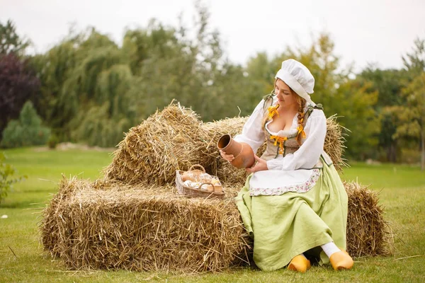 Mulher camponesa senta-se no feno e derrama leite — Fotografia de Stock