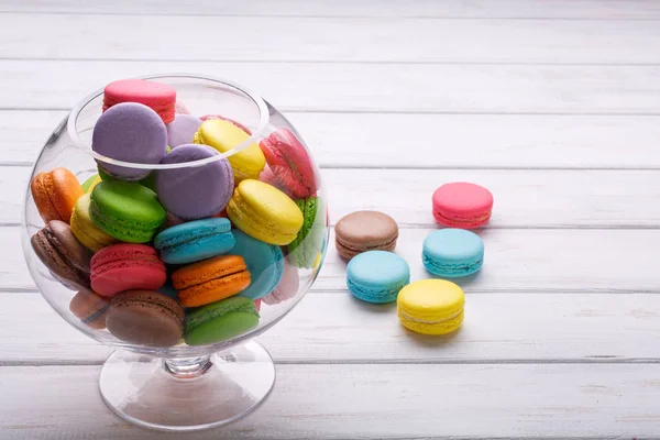 Macarons colorés dans un vase en verre sur table en bois blanc — Photo