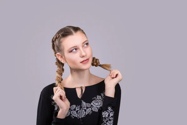 Mujer joven con elegantes coletas de peinado. Chica expresiva en un bordado negro sobre fondo gris —  Fotos de Stock