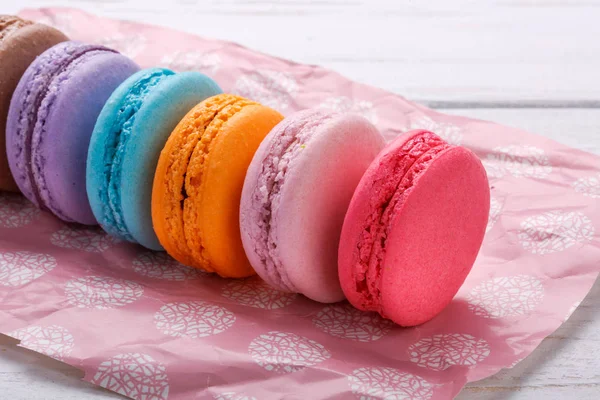 Macarons français doux et colorés ou macaron sur papier rose sur fond de bois blanc — Photo