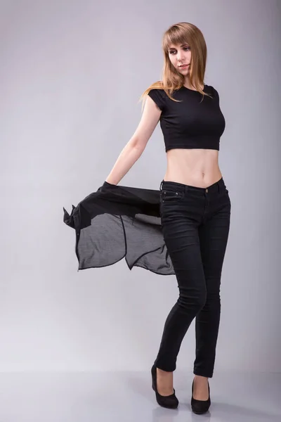 Beautiful young casual girl taking off black shirt wearing black top. Full body length standing portrait over gray background. — 图库照片