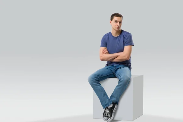 Young man sitting on white cube. isolated — Stock Photo, Image