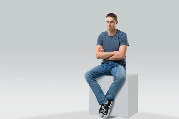 Young man sitting on white cube. isolated — Stock Photo, Image