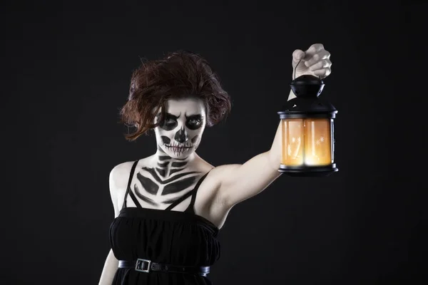 Scary woman with lantern over black background - Spooky image of a scary woman with dark eyes and appearance of a witch, in a white dress, holding a lit lantern, in a dark night atmosphere. — Stock Photo, Image