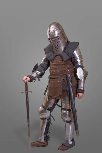 Cavaleiro blindado em um capacete e com uma espada sobre fundo cinza . — Fotografia de Stock