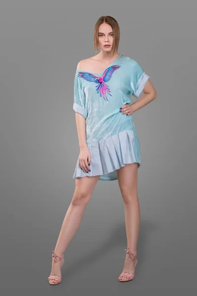 Mooi meisje met professionele make-up gekleed in een kleine elegante blauwe jurk met een papegaai op een grijze achtergrond. — Stockfoto