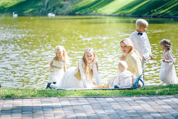 Grandmother and grandchildren enjoying picnic in a park. Grandma playing with children in a sunny summer forest. Summer outdoor fun in the garden. Grandparents and kids on a meadow. — Stock Photo, Image