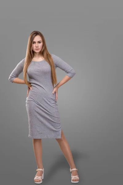 Een mooi meisje met lange haren draagkracht in licht grijze jurk, geïsoleerd over grijze achtergrond — Stockfoto