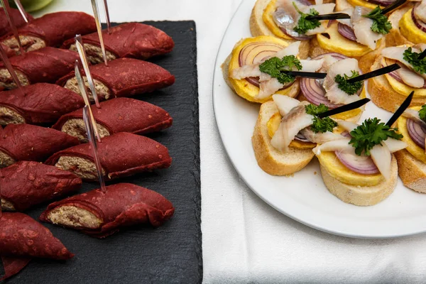 Två plattor med snacks på ett buffébord. Urval av välsmakande bruschetta eller kanapéer på rostad baguette med potatis sill fisk, röd lök. — Stockfoto