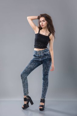güzel uzun bacakları çok seksi kadın modeliyle portresi kameraya gri arka plan üzerinde seyir poz ayakta giyen denim kot pantolon siyah iç çamaşırı üst,