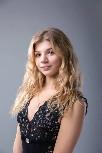 Porträtt av vacker blond tonårstjej i svart klänning över grå — Stockfoto