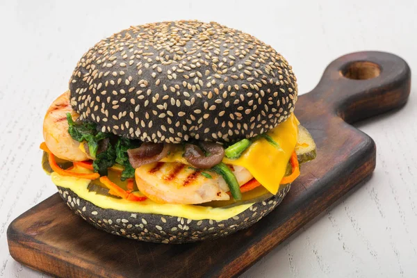 Black burger with fish, cheese, pickle, carrot, spinach sprinkled with sesame seeds — Stock Photo, Image