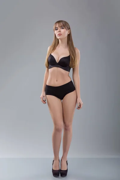 Mujer impecable en bikini negro sobre fondo gris. Foto de chica con cuerpo delgado tonificado. Concepto de belleza y cuidado corporal —  Fotos de Stock