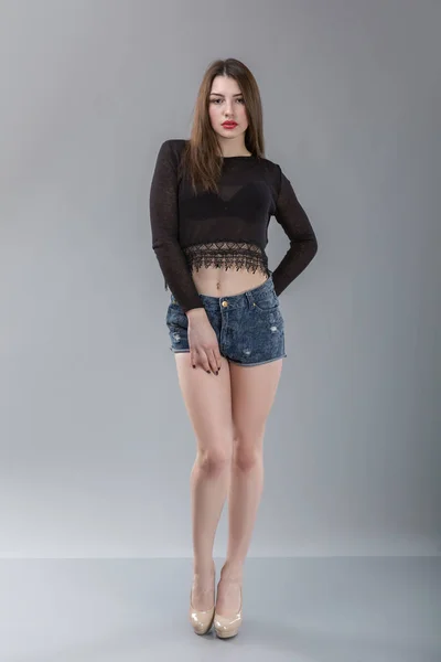 Jolie femme sexy modèle avec un corps incroyable, de longues jambes, portant des shorts en denim bleu, haut noir. Fond gris clair — Photo