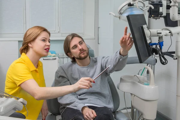Le dentiste montre une radiographie du patient. Concept de soins dentaires. L'inspection dentaire est donnée à un bel homme entouré d'un dentiste — Photo