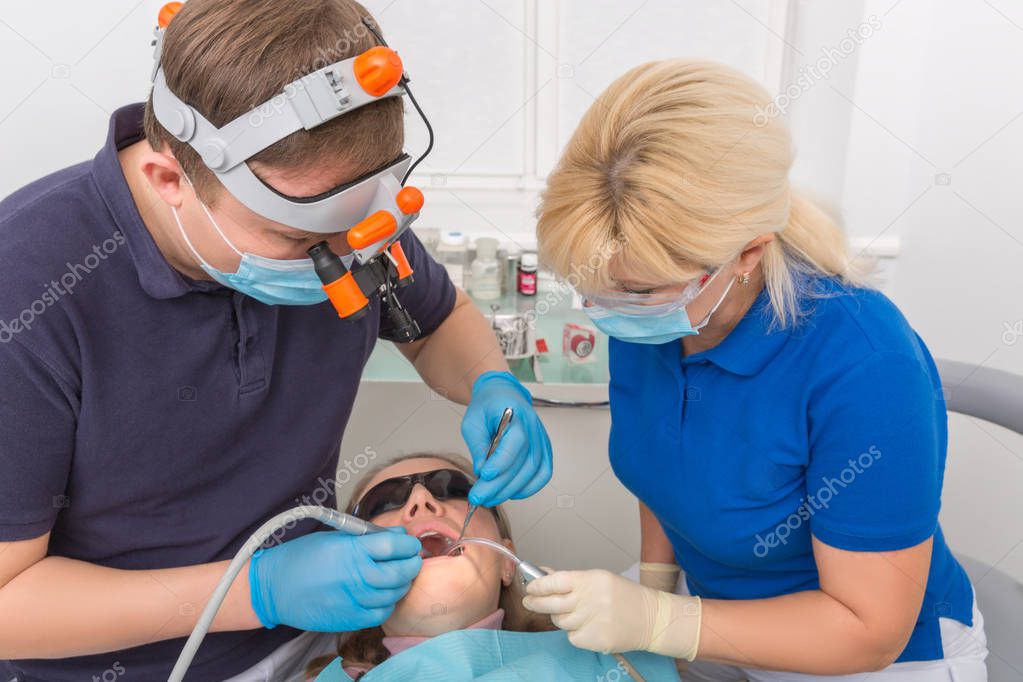 Dentist in mask with loupe binocularsand assistant working on patient