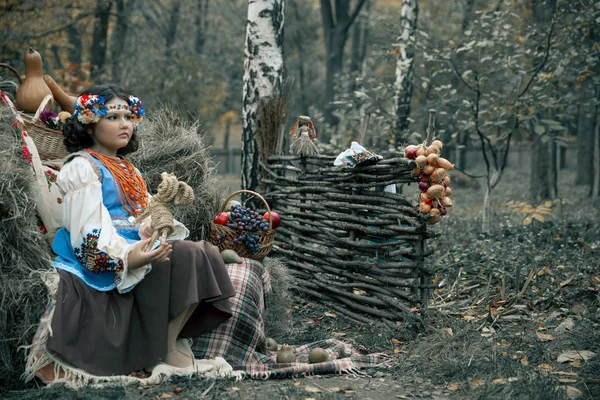 Dospívající dívka sedící v seně věnec a národní ukrajinské kostým vedle košík s ovocem — Stock fotografie