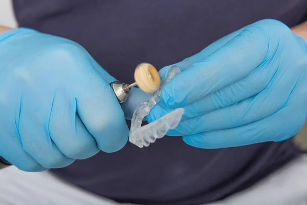 Close up on dentist hands covered with latex gloves shaping mouth guard with file equipment