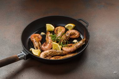 karanlık bir taş zemin üzerine siyah bir tavada karides karides sarımsak, limon, baharatlar ve maydanoz garnitür