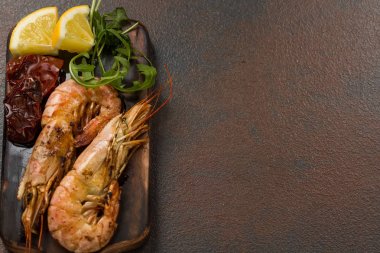 Fried kaplan karides ile limon, kurutulmuş domates ve yeşillik veya rukkola koyu ahşap kesme tahtası.