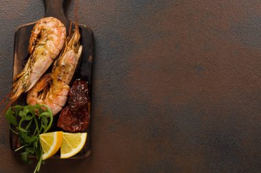 Fried kaplan karides ile limon, kurutulmuş domates ve yeşillik veya rukkola koyu ahşap kesme tahtası.