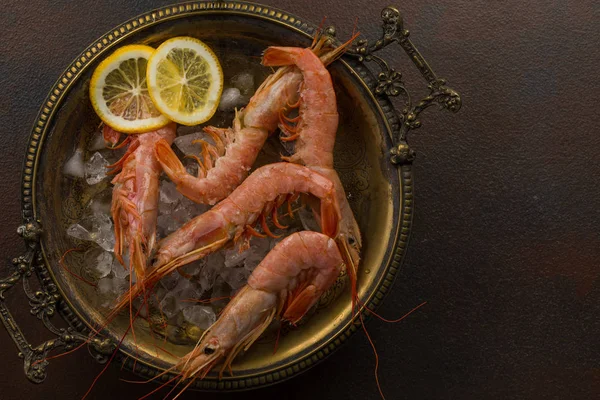 Grandes crevettes tigrées au citron et glaçons sur plaque ancienne sur fond de pierre sombre. Vue de dessus sur une collation appétissante aux fruits de mer — Photo