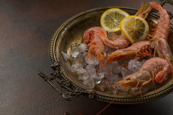 Camarones tigre grandes con limón y cubitos de hielo en el plato antiguo sobre fondo de piedra oscura. vista sobre apetitoso aperitivo de mariscos —  Fotos de Stock